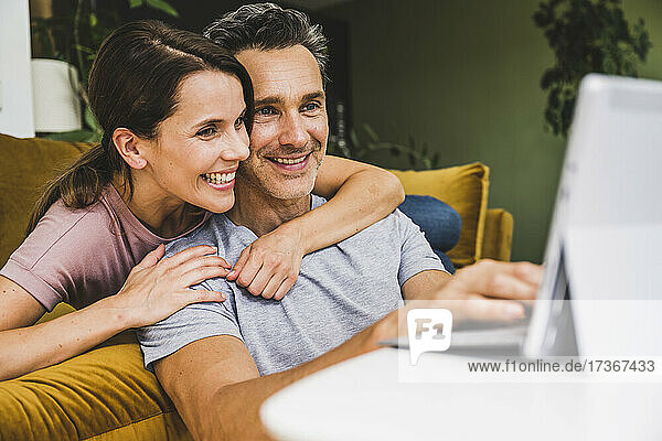 Frau umarmt Mann bei der Nutzung eines digitalen Tablets zu Hause