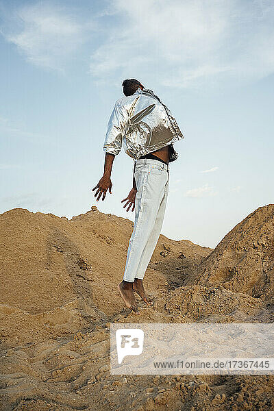 Mann mit silberner Jacke springt auf Sand