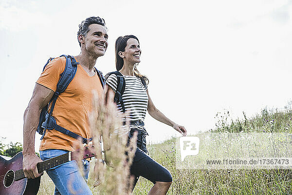 Couple with backpacks smiling while walking on grass
