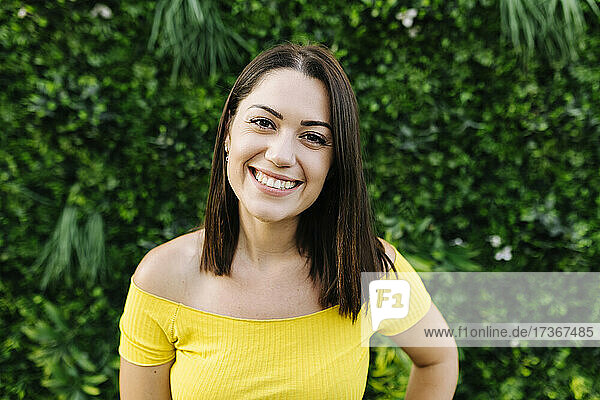 Smiling young woman in front of hedge