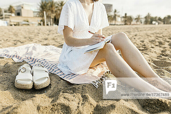 Frau  die am Strand sitzend in ein Buch schreibt