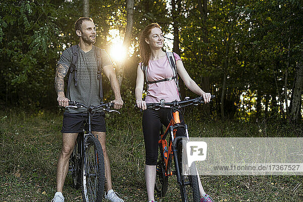 Lächelndes junges Paar steht mit Fahrrädern im Wald