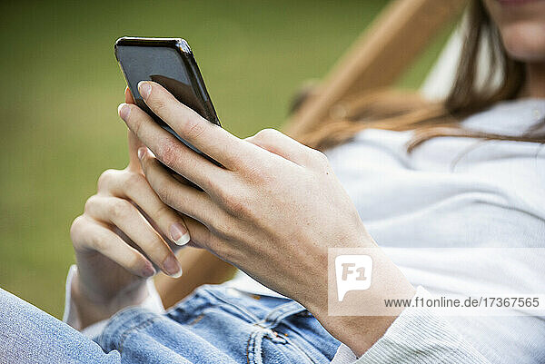 Mittelteil einer jungen Frau  die im Park ein Smartphone benutzt