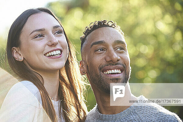 Nahaufnahme eines lächelnden jungen Paares  das in einem öffentlichen Park wegschaut