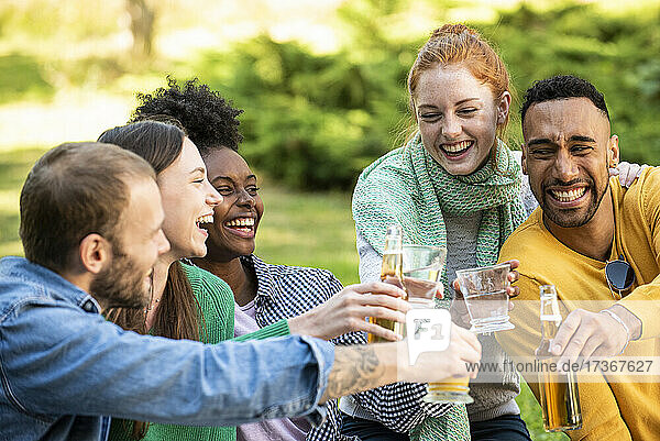 Fröhliche junge Freunde stoßen mit Getränken im Garten an