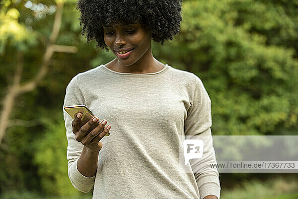 Lächelnde junge Frau mit Smartphone im Park