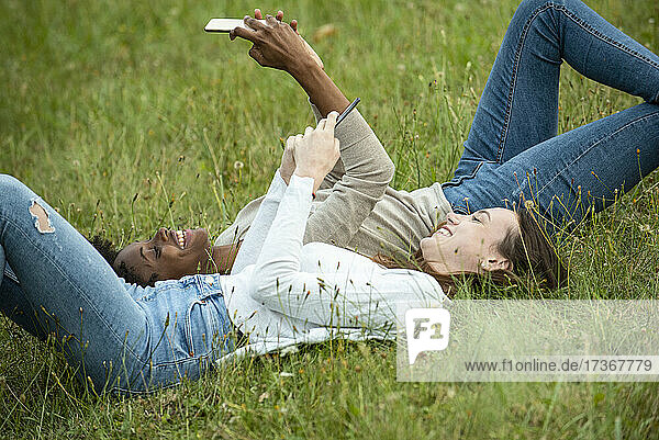 Junge Freundinnen liegen im Gras und benutzen ein Smartphone im Park