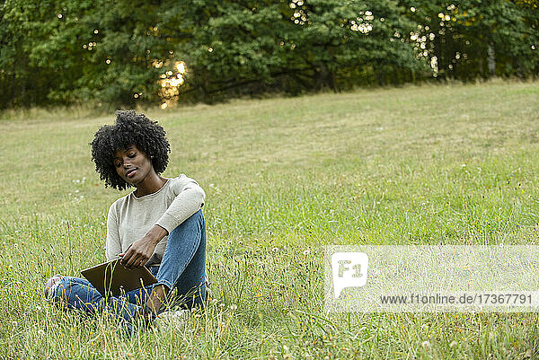 Smiling young woman using digital tablet in public park