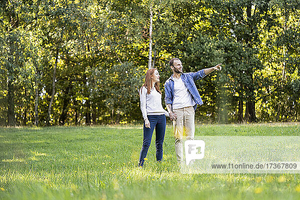 Lächelnder junger Mann  der seinem Partner etwas zeigt  während er im Park steht
