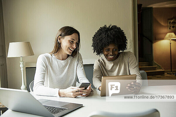 Lächelnde junge Frauen  die zu Hause ein digitales Tablet und ein Smartphone benutzen