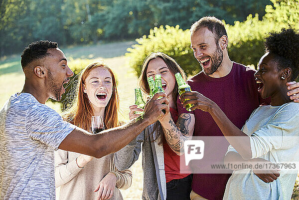 Glückliche junge Freunde stoßen im Garten mit Bierflaschen an