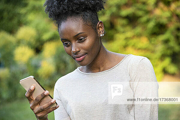 Nahaufnahme einer lächelnden jungen Frau  die im Park ihr Smartphone benutzt
