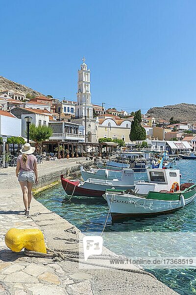 Touristin mit Sonnenhut  Fischerboote im Hafen von Chalki mit türkisblauem Wasser  Promenade mit bunten Häusern des Ortes Chalki  Chalki  Dodekanes  Griechenland  Europa