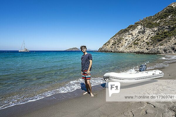 Young man with dinghy on a beach in Gyali  sailing boat behind  Dodecanese  Greece  Europe