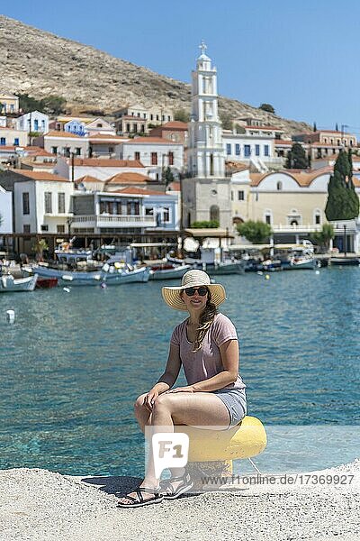 Touristin mit Sonnenhut  Hafen von Chalki mit türkisblauem Wasser  Promenade mit bunten Häusern des Ortes Chalki  Chalki  Dodekanes  Griechenland  Europa