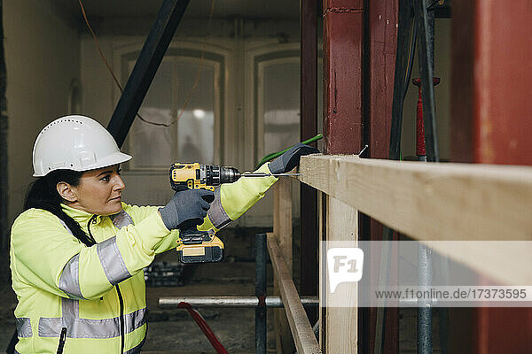 Weiblicher Arbeiter bei der Arbeit auf einer Baustelle mit einer Bohrmaschine auf einer Holzplanke