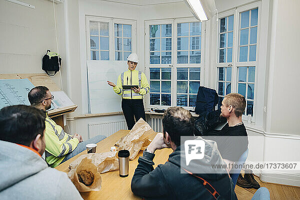 Bauunternehmerin mit digitalem Tablet diskutiert mit männlichen Kollegen bei der Planung im Büro