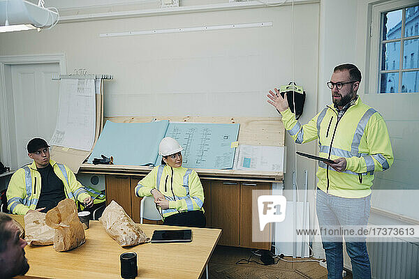 Männlicher Bauunternehmer gestikuliert bei einer Diskussion mit Kollegen im Büro