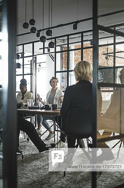 Female entrepreneur discussing with colleagues seen through doorway of startup company