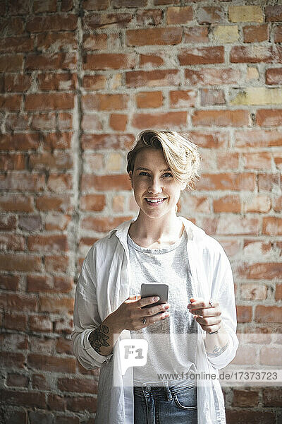 Smiling female hacker with smart phone in startup company