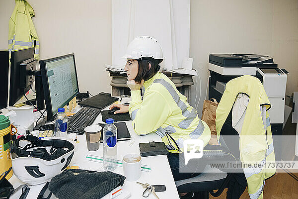 Seitenansicht eines weiblichen Ingenieurs  der mit der Hand am Kinn sitzt  während er im Büro am Computer arbeitet