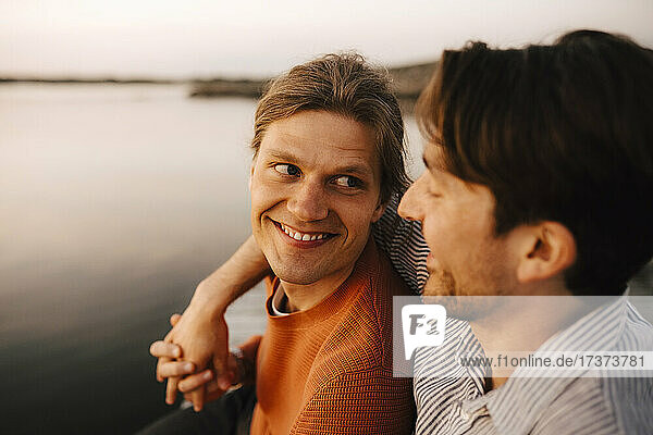 Smiling man with arm around of boyfriend by lake