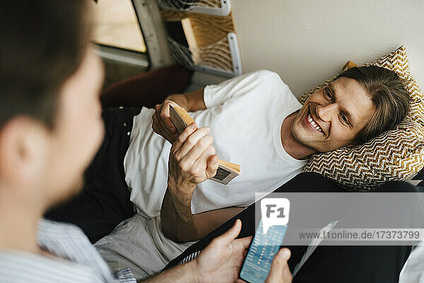 Mann hält ein Buch in der Hand  während er seinen Freund beim Benutzen eines Smartphones im Wohnmobil beobachtet