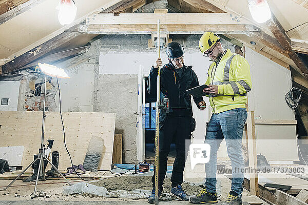 Full length of male construction workers discussing over digital tablet while working at site