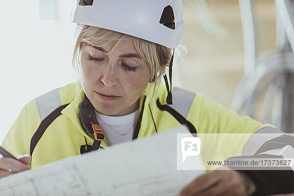 Female builder analyzing floor plan while working at construction site