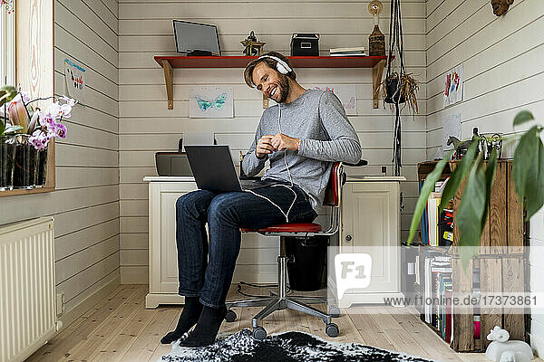 Lächelnder Mann in voller Länge  der Kopfhörer trägt  während er einen Videoanruf über einen Laptop zu Hause führt