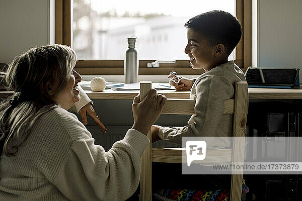Smiling son talking with mother while sitting on chair at home