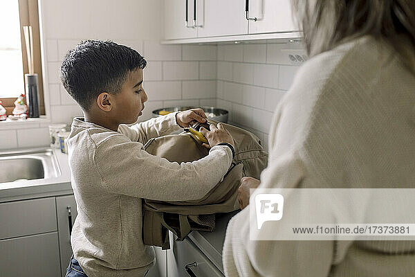 Autistischer Junge  der zu Hause bei seiner Mutter eine Banane in die Tasche steckt