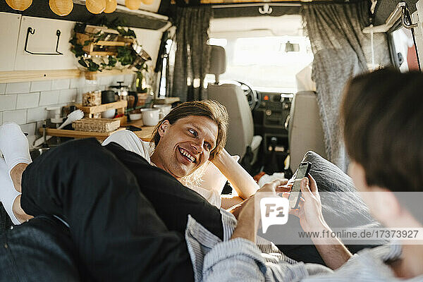 Mid adult man sharing smart phone with boyfriend in camping van