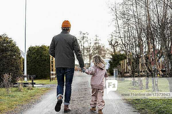 Rückansicht in voller Länge  Vater und Tochter halten sich an den Händen  während sie auf der Straße gehen
