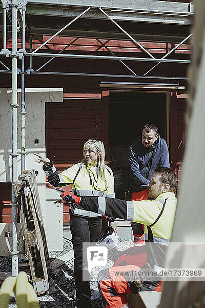 Weiblicher Bauunternehmer mit männlichem Kollegen  der an einem sonnigen Tag auf eine Baustelle zeigt