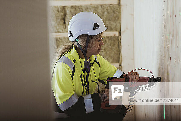 Female builder using work tool on wall while working at construction site