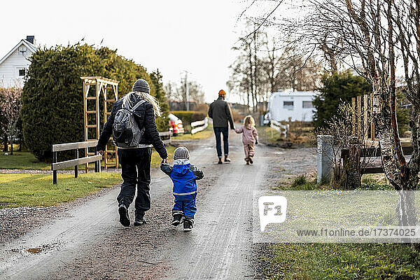 Full length rear view of mother and son holding hands while walking on road