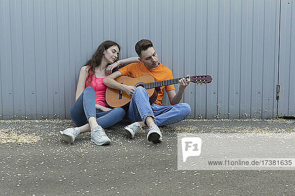 Junges Paar spielt Gitarre an der Wand