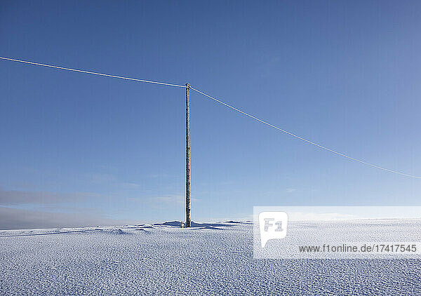 Hölzerner Strommast auf leerer  schneebedeckter Landschaft. Elektroindustrie  Stromleitung.