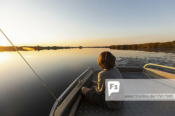 Young boy fishing at the stern of a boat on flat calm water
