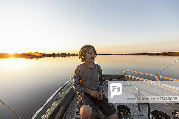 A boy on the deck of a small boat on the Okavango Delta at sunset  Botswana.