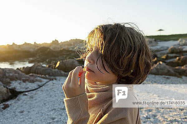 A boy on the beach at sunset  having a snack.