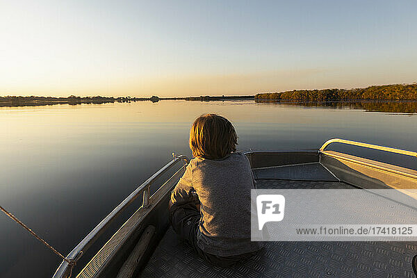 Young boy sitting at the stern of a boat on flat calm water