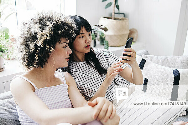 Woman using mobile phone while sitting with friend at home