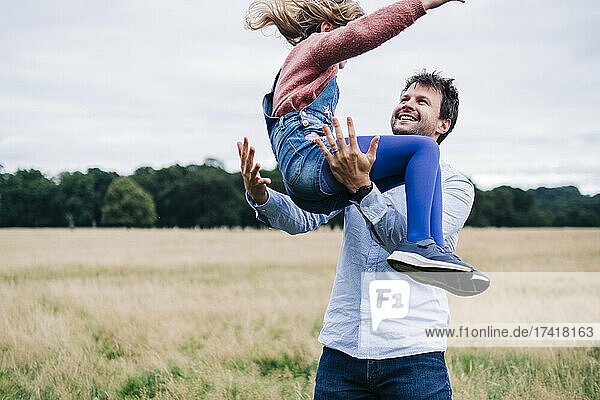 Happy father playing with daughter on meadow