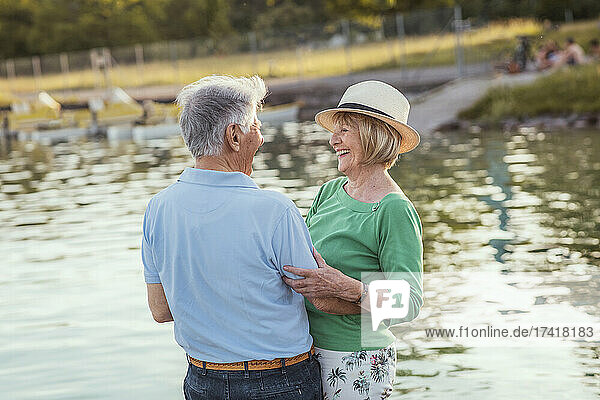 Cheerful senior couple looking at each other while standing by lake