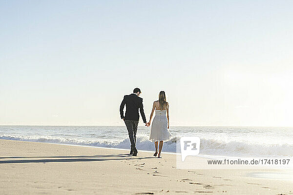 Frischvermähltes Paar hält Händchen beim Spaziergang am Strand