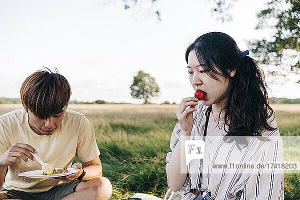 Woman eating strawberry while sitting with man at park during picnic