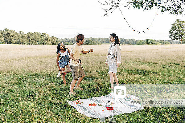 Happy friends dancing on meadow during picnic