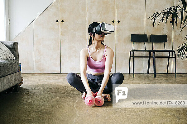 Woman with virtual reality headset and dumbbells sitting on floor